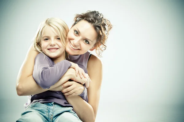 Beautiful brunette woman with young blond girl on grey background — Stock Photo, Image