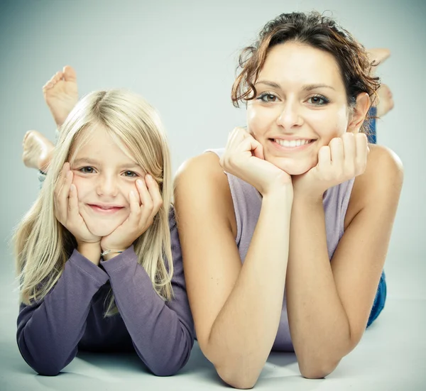 Beautiful brunette woman with young blond girl on grey background — Stock Photo, Image