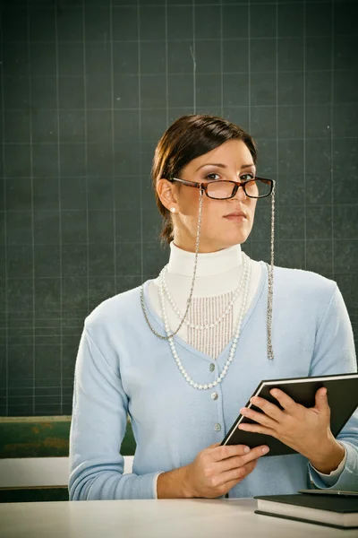 Schöne ernsthafte junge Lehrerin mit Brille und Blackbouard — Stockfoto