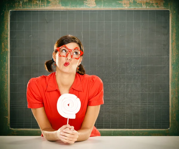 Sensuele jonge student rood gekleed met glazen eten snoep en blackboard — Stockfoto