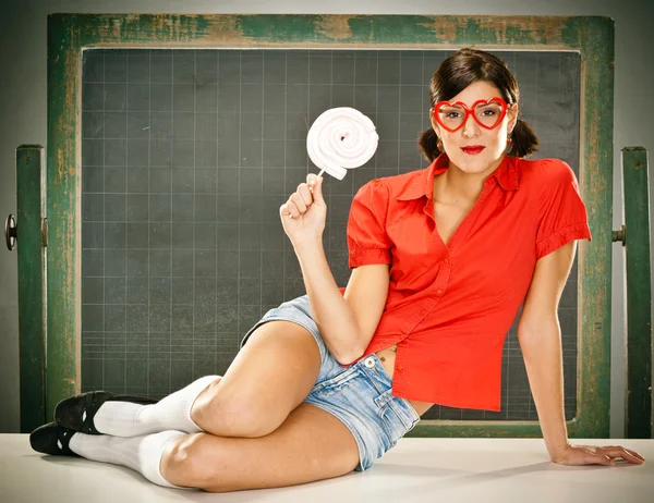 Sensuale giovane studente rosso vestito con occhiali mangiare caramelle e lavagna — Foto Stock