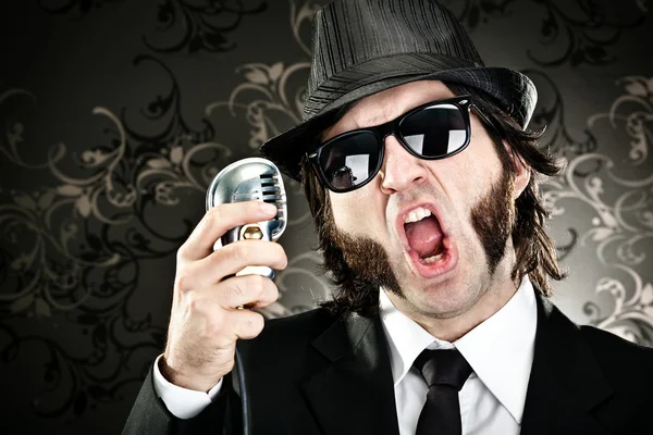 Κομψό αφεντικό άνδρας με γυαλιά ηλίου και πορτρέτο τραγούδι μικρόφωνο σε μαύρο φόντο — Φωτογραφία Αρχείου
