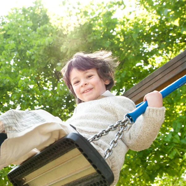 Schöne männliche Kind spielen auf Schaukel in einem Park — Stockfoto