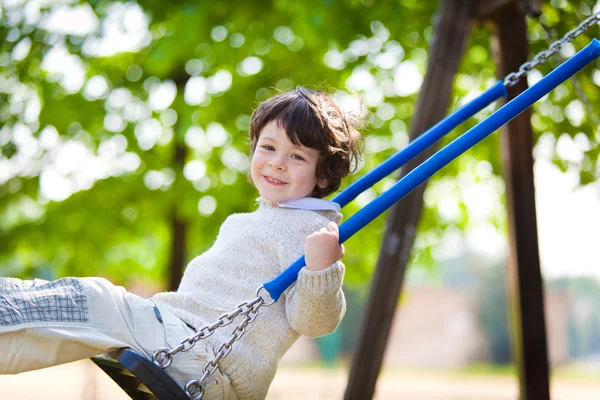 Bonito menino masculino jogar no balanço em um parque — Fotografia de Stock