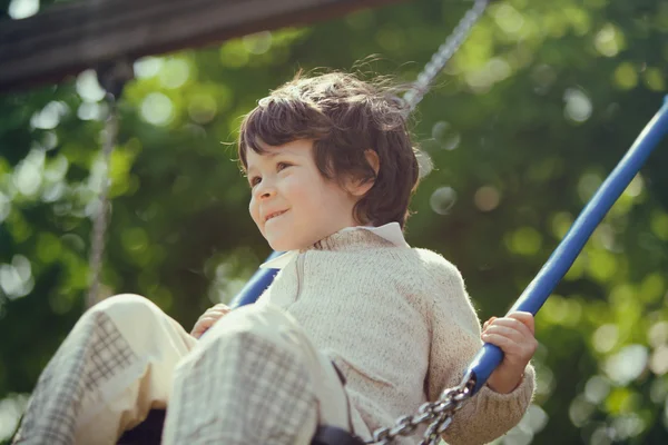 Beautiful male kid play on swing in a park — Stock Photo, Image