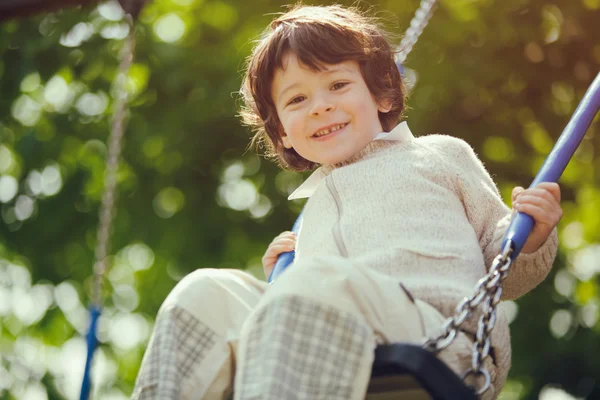 Beautiful male kid play on swing in a park — Stock Photo, Image