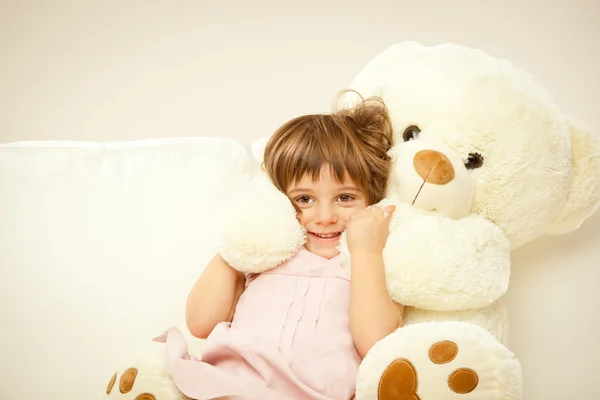 Blonde vrouwelijke kind spelen met haar witte teddy beer in een bed — Stockfoto