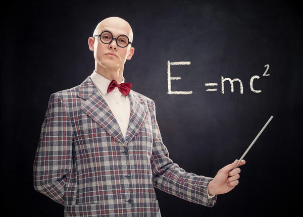 Bald caucasian professor or teacher with bow tie and glasses point stick on blackboard with Einstein formula — Stock Photo, Image