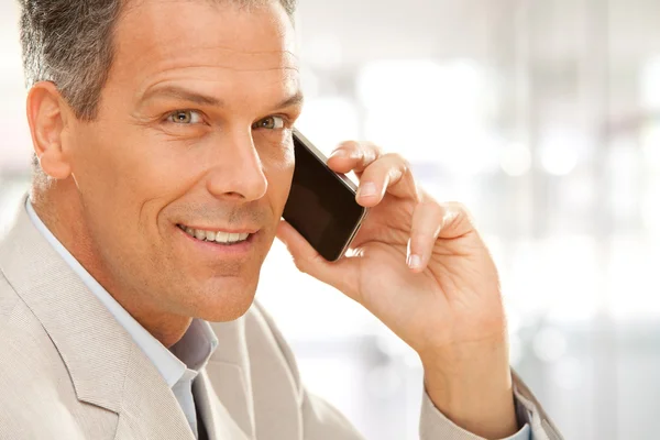 Красивый улыбающийся бизнесмен разговаривает по телефону в офисе — стоковое фото