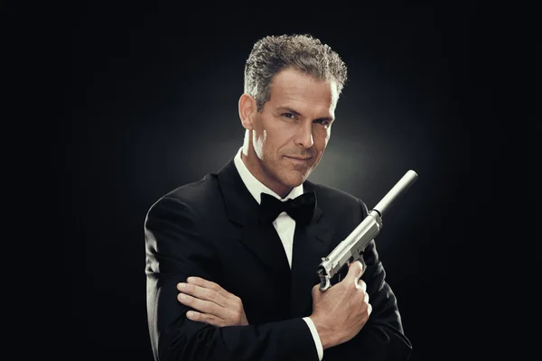 Elegant man with bow tie and gun isolated on black — Stock Photo, Image