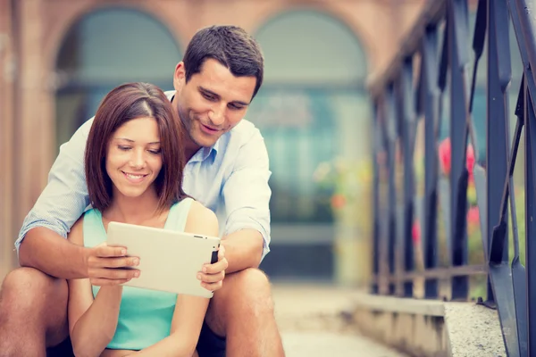 Joven morena pareja divirtiéndose junto con tableta en parque — Foto de Stock