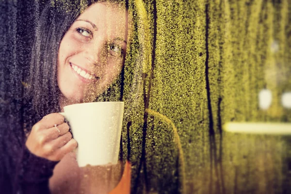 お茶のカップを持つロマンチックな若い女性が窓から雨を見てください。 — ストック写真