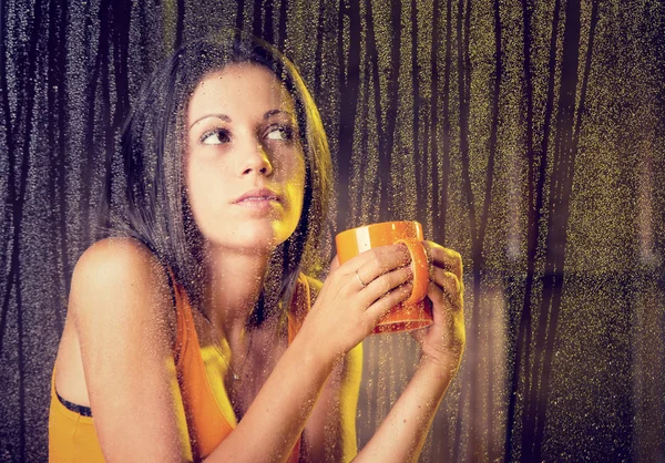 Csésze tea romantikus fiatal nő úgy néz ki, az eső az ablakon — Stock Fotó
