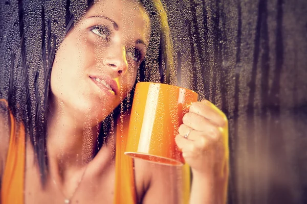 Romántica joven con taza de té mira a la lluvia a través de la ventana — Foto de Stock