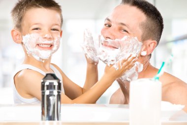 happy child have fun with dad with shaving foam in the bathroom clipart