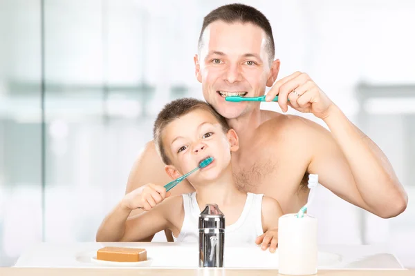 Sorrindo criança escova os dentes com o pai no banheiro — Fotografia de Stock