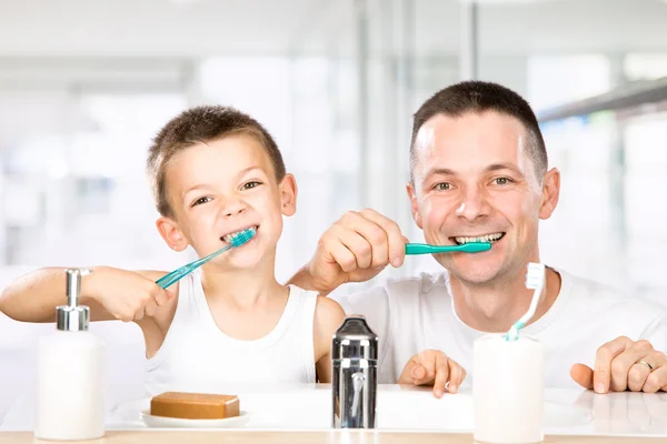 Sorrindo criança escova os dentes com o pai no banheiro — Fotografia de Stock
