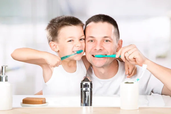 Sorrindo criança escova os dentes com o pai no banheiro — Fotografia de Stock