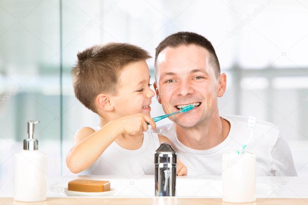 Smiling child brushes his teeth with dad in the bathroom Stock Photo by