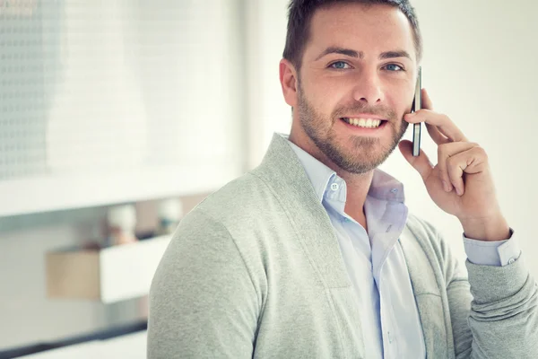 Gülümseyen genç casual işadamı ofisinde telefonda konuşuyor — Stok fotoğraf
