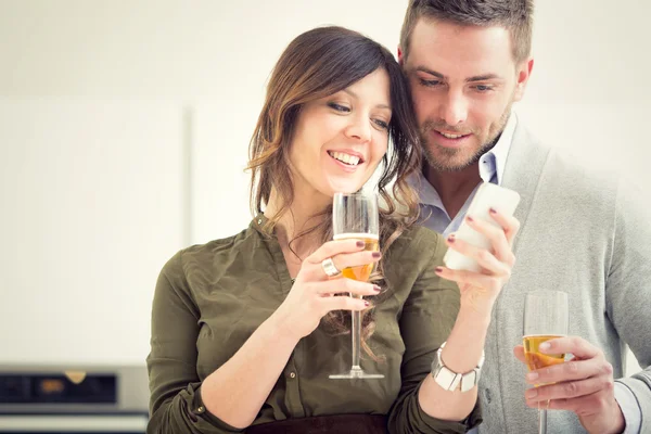 Joven pareja casual vítores con champán y teléfono en la cocina — Foto de Stock