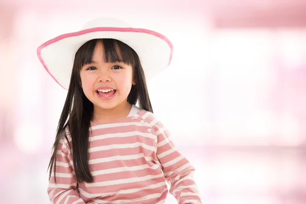 Asiatico sorridente bambina con cappello su sfondo rosa — Foto Stock