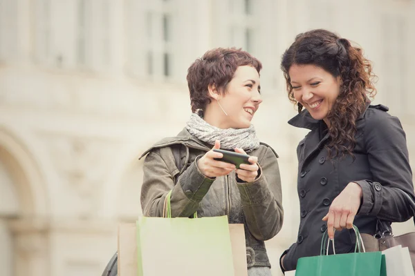 O par de mulheres faz compras em conjunto com o telefone na paisagem urbana — Fotografia de Stock