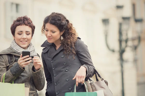 O par de mulheres faz compras em conjunto com o telefone na paisagem urbana — Fotografia de Stock