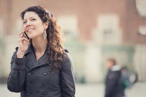 Sorridente donna riccia che parla al telefono nel paesaggio urbano — Foto Stock