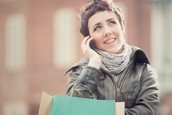 Pelo corto sonriente tienda de mujer con teléfono en paisaje urbano — Foto de Stock