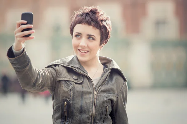 Pelo corto mujer sonriente tomar selfie en paisaje urbano — Foto de Stock