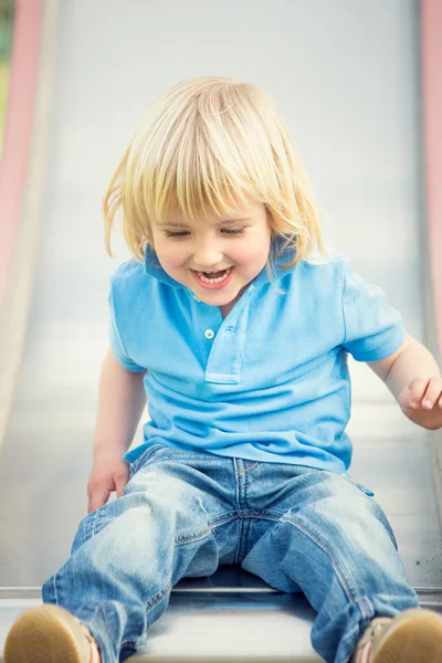 Gelukkig lachend blond kind spelen met dia in een park — Stockfoto