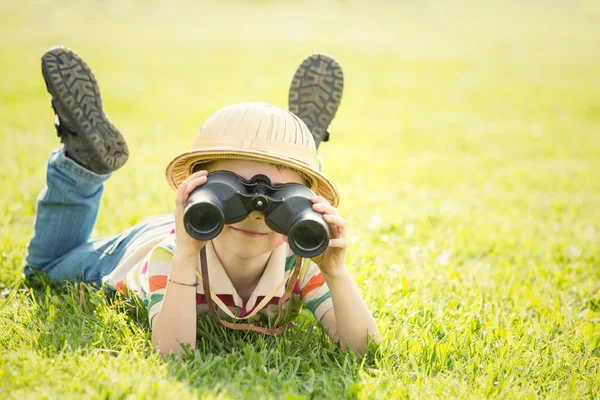 Счастливый улыбающийся ребенок в шляпе играет в бинокль в саду — стоковое фото