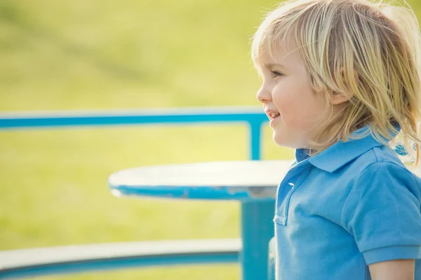 Felice sorridente bambino biondo giocare con giostra in un parco — Foto Stock