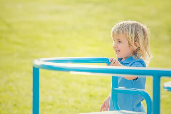 Feliz sonriente niño rubio jugar con carrusel en un parque —  Fotos de Stock
