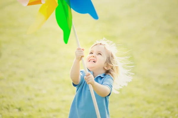 Feliz sorrindo criança loira brincando com pinwheel em um parque — Fotografia de Stock