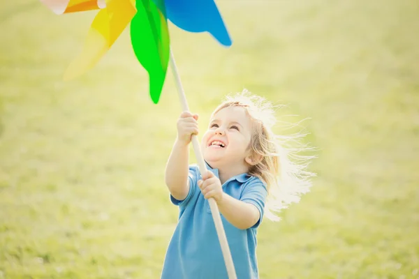 Gelukkig lachend blond kind spelen met pinwheel in een park — Stockfoto