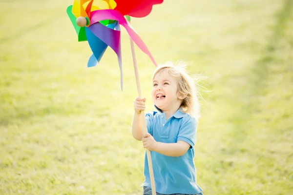 Felice sorridente bambino biondo giocare con girandola in un parco — Foto Stock