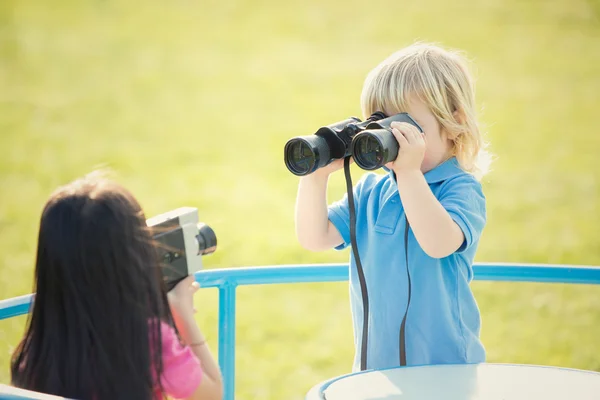 Couple of interracial children play with binocular in a garden — Stock Photo, Image