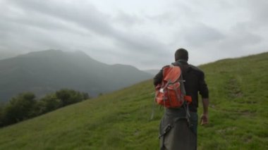 Genç adam bir kırmızı vintage sırt çantası ile açık dağ yolu üzerinde yürüyor