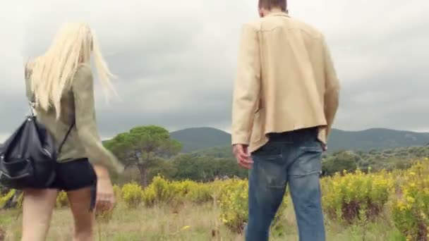 Visão traseira da bela jovem loira e homem casal apaixonado caminha ao ar livre na natureza — Vídeo de Stock