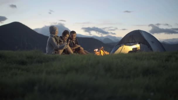 Grupo de três amigos aquecendo com fogo de acampamento na natureza montanha ao ar livre — Vídeo de Stock