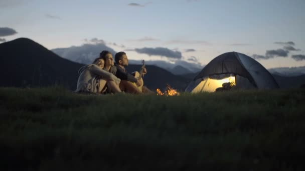3 つの友人の演劇のギターのグループし、自然山でキャンプの火で歌う — ストック動画