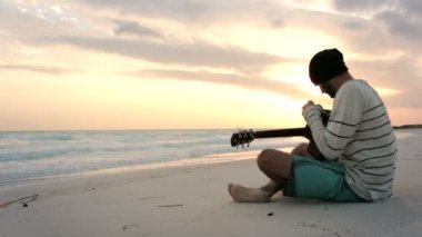 Genç güzel adam gitar okyanus plaj sahil, güneş doğarken tunes.