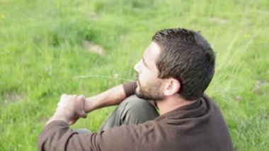 Çimenlerin üzerinde oturan genç güzel adam panorama adlı günbatımında izliyor