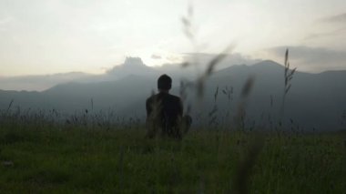 Genç adam çimlere oturmuş panorama adlı günbatımında izliyor