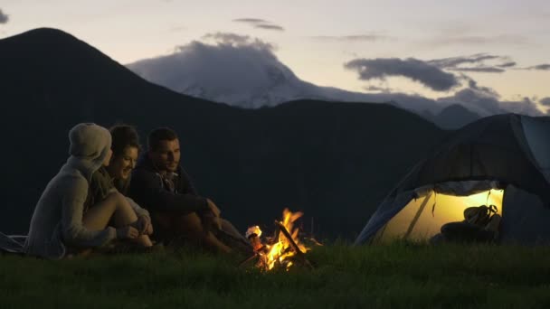 Gruppo di tre amici che si scaldano con il fuoco del campo nella natura montagna all'aperto — Video Stock