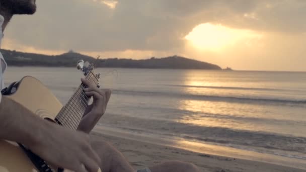 Νέοι όμορφη άνθρωπος κάθεται εξωτερική στην ακτή παίζουν κιθάρα — Αρχείο Βίντεο