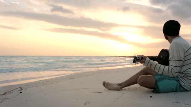 Mooie jongeman speelt gitaar bij oceaan strand aan zee bij zonsopgang — Stockvideo