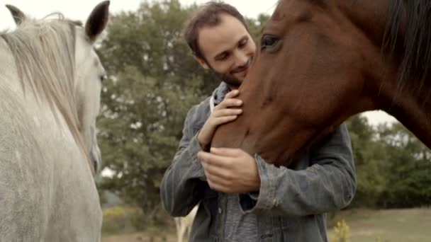 Joven golpe de hombre y abraza un caballo marrón al aire libre — Vídeo de stock